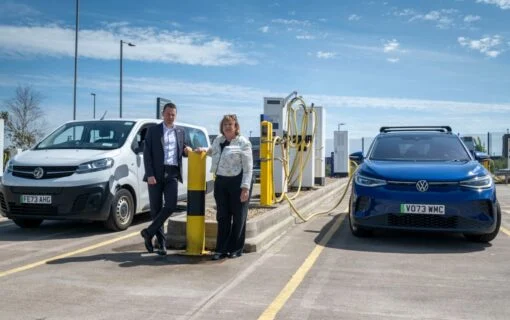 a white man and woman stand next to eachother near ev chargers.