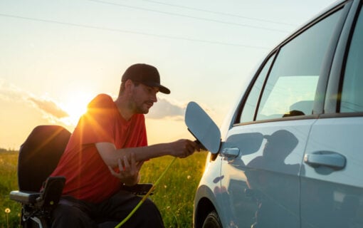 Man in wheelchair plugging in a charger in an electric car. Image: AdobeStock