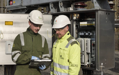 Two men in high vis jackets stand by a large fuse box