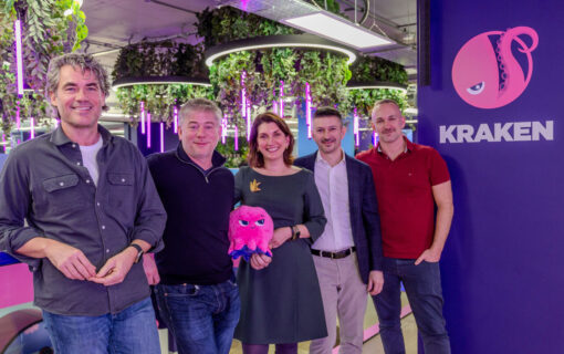 Kraken staff in front of Kraken Technologies branding board with one holding an Octopus Energy plush toy.