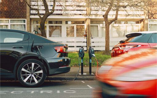 Two cars plugged into an EV chargepoint as one, blurred from speed, drives past