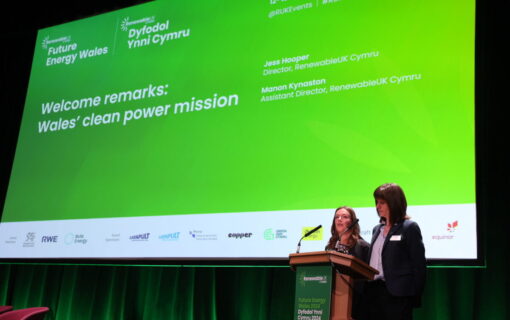 Two women stand in front of a large screen as they present a report at a conference
