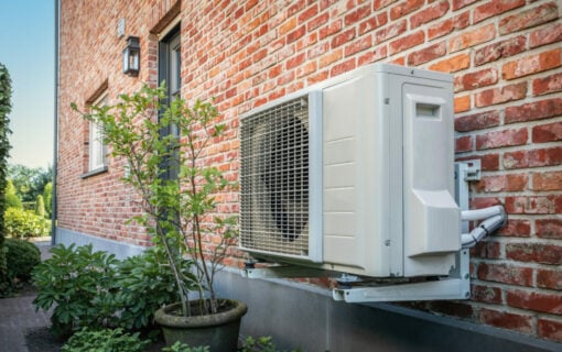 Domestic heat pump unit mounted on a brick house wall.