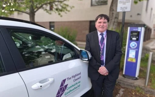 A man stands next to a white car with the highland council logo