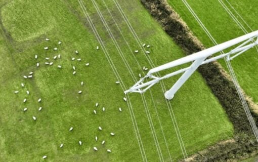 an overhead shot of a pylon on green fields with sheep