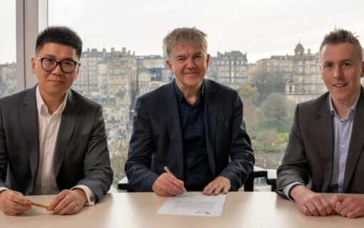 Three men in suits sit at a table and smile at the camera