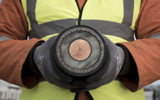 Two hands hold a large interconnector cable, cut so the cross section can be seen
