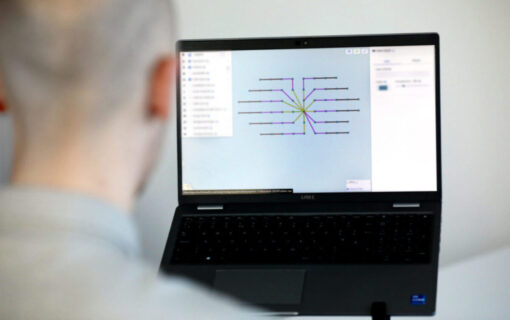 A man, out of focus and with his back to the camera, uses cable planning software on a laptop
