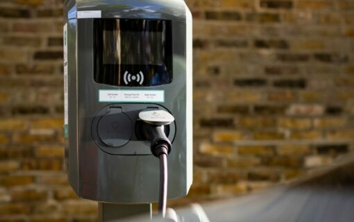 Public EV car charger on street with brick wall in the background and car in the foreground