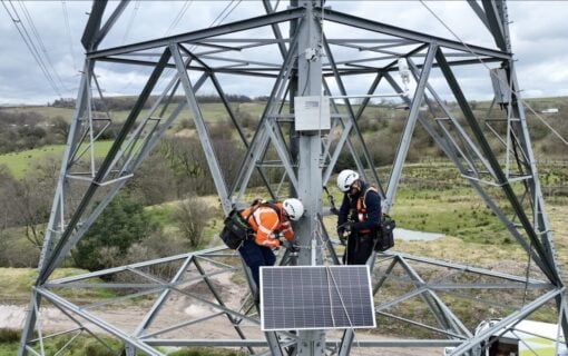 workers install a sensor with a solar panel on a transmission tower