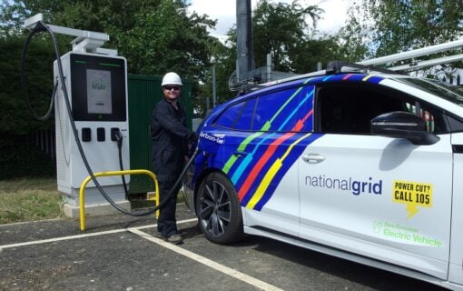 a man in black overalls and a white helmet plugs an EV charger into a National Grid branded EV