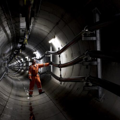 a person in a high vis vest inspects cables in a large tunnel