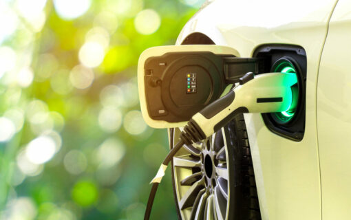 Yellow EV car plugged into charger with greenery in the background