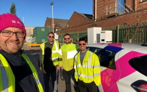 men in high vis jackets stand by a pink and white car