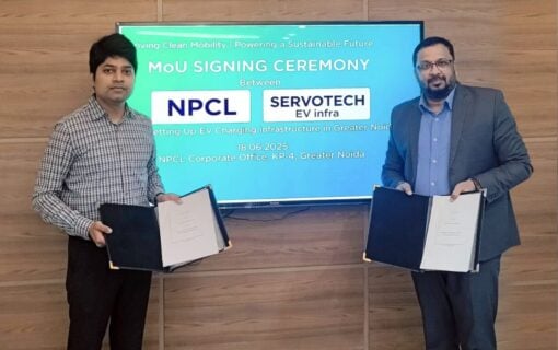Two Indian men stand in front of a screen with documents in hand