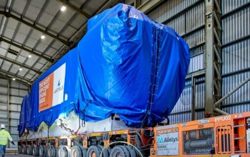 A large truck carries an engine covered by blue tarpaulin