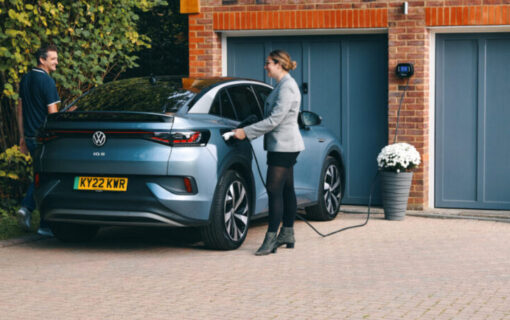 a woman charges an EV in front of a home garage