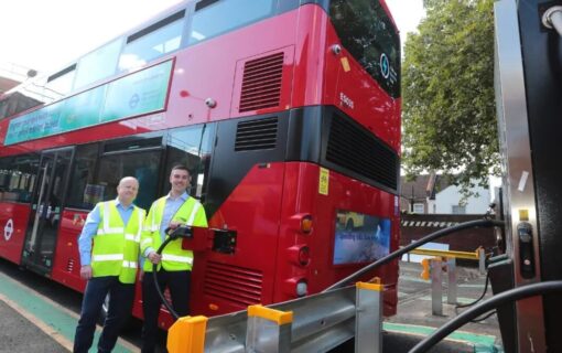 Two men in high vis stand next to an electric london bus