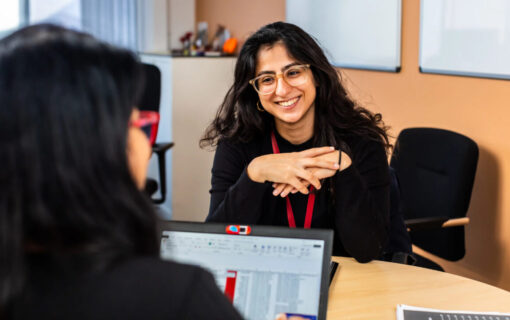 two west Asian women look at eachother over laptop screens while smiling