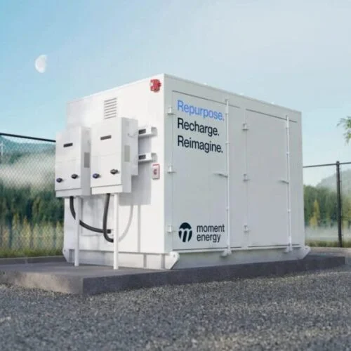a battery energy storage unit painted white and bearing the moment energy logo stands alone and outside