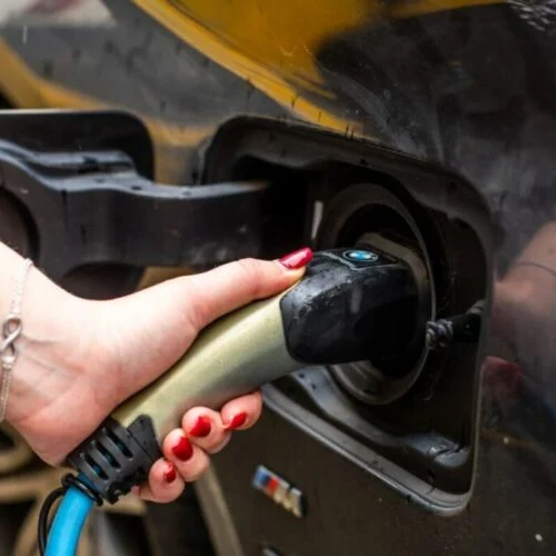 a hand plugging an ev charger into a car