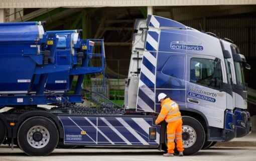 a man stands next to a large blue lorry.