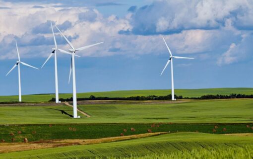 Wind turbines on rolling green hills under a bright blue sky with white clouds