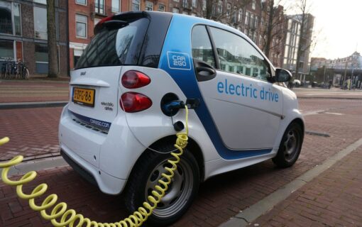 an electric smart car plugged in to charge with a yellow cable