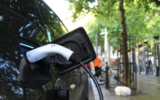 An electric car is plugged into a charger on a leafy street