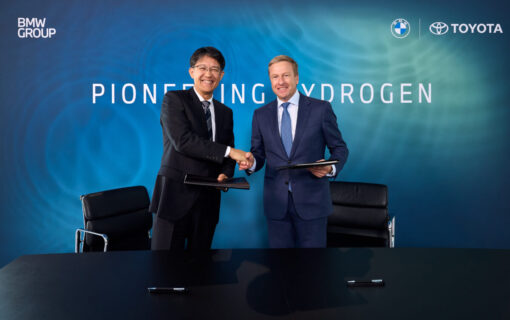 An Asian man and a white man shake hands in front of a blue background after a successful business deal