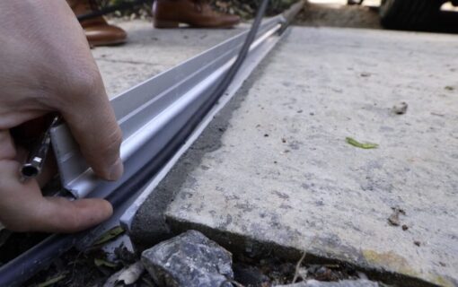A hand lays a thin cable into a metal channel set into the ground