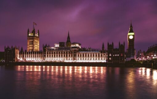 The houses of parliament lit up at night in front of a purple-tinged sky