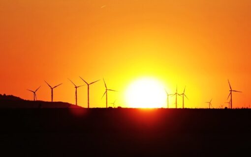 Wind turbines on a hill in the distance, silhouetted against an orange sunset