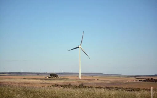 A single wind turbine on a hill underneath a blue sky
