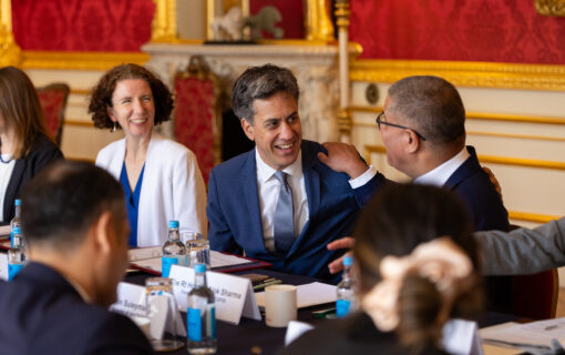 ed miliband smiles surrounded by people in a red room