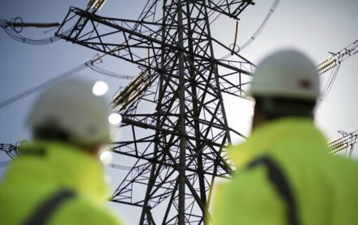 two people in high vis, out of focus, stare up at a transmission tower