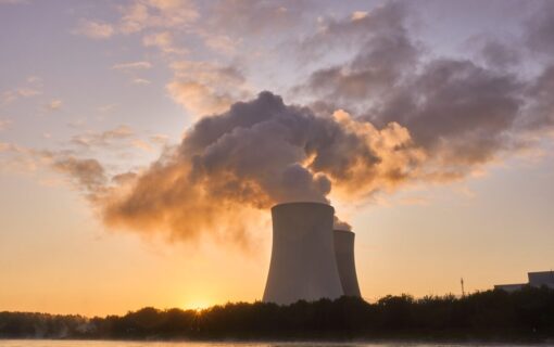 a nuclear cooling tower with steam pouring out of it, at sunset