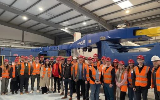 A group of people in hard hats and hi vis vests stand near industrial equipment