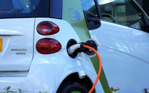 a white electric car plugged into an orange charging cable