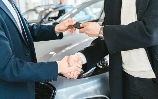 A Person Giving a Car Key To Another Person While Shaking His Hands