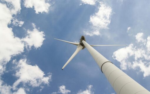 A white wind turbine, shot from below, under a blue sky