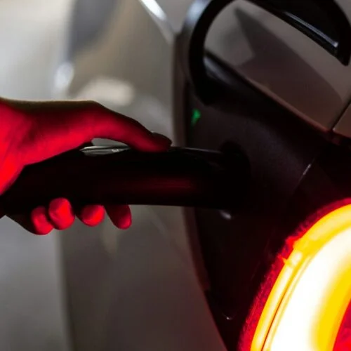 a hand, lit by red light, plugs a car into an EV charger
