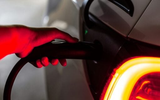 a hand, lit by red light, plugs a car into an EV charger