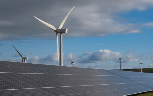 Solar panels sit in front of a wind turbine