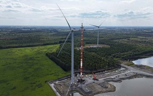 A wind turbine stands next to a crane working to install it.