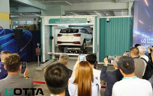 a group of people watch a car lifted into a battery swapping machine