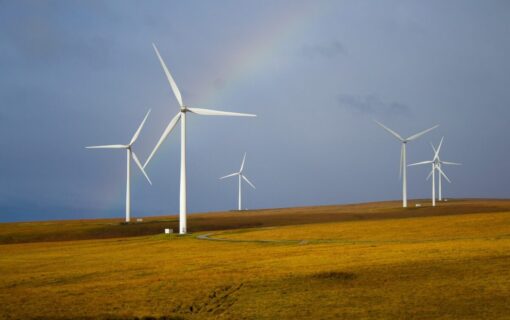 Four wind turbines spread across a hillside with a rainbow behind