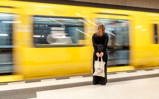 A woman stands in front of a bright yellow subway train