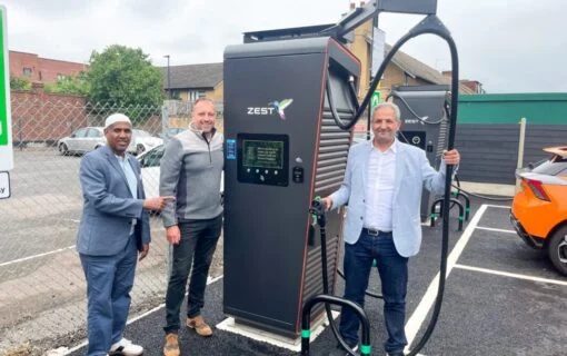 Three men pose next to a large Zest-branded EV charger